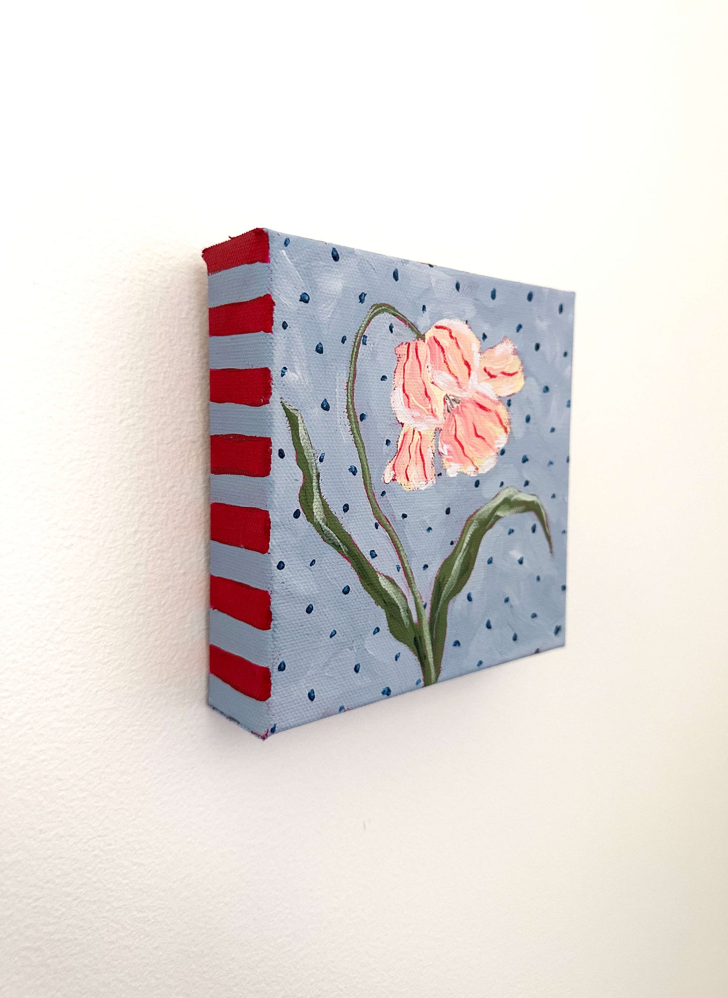 Canvas painting of a pink flower with red stripes on a blue background