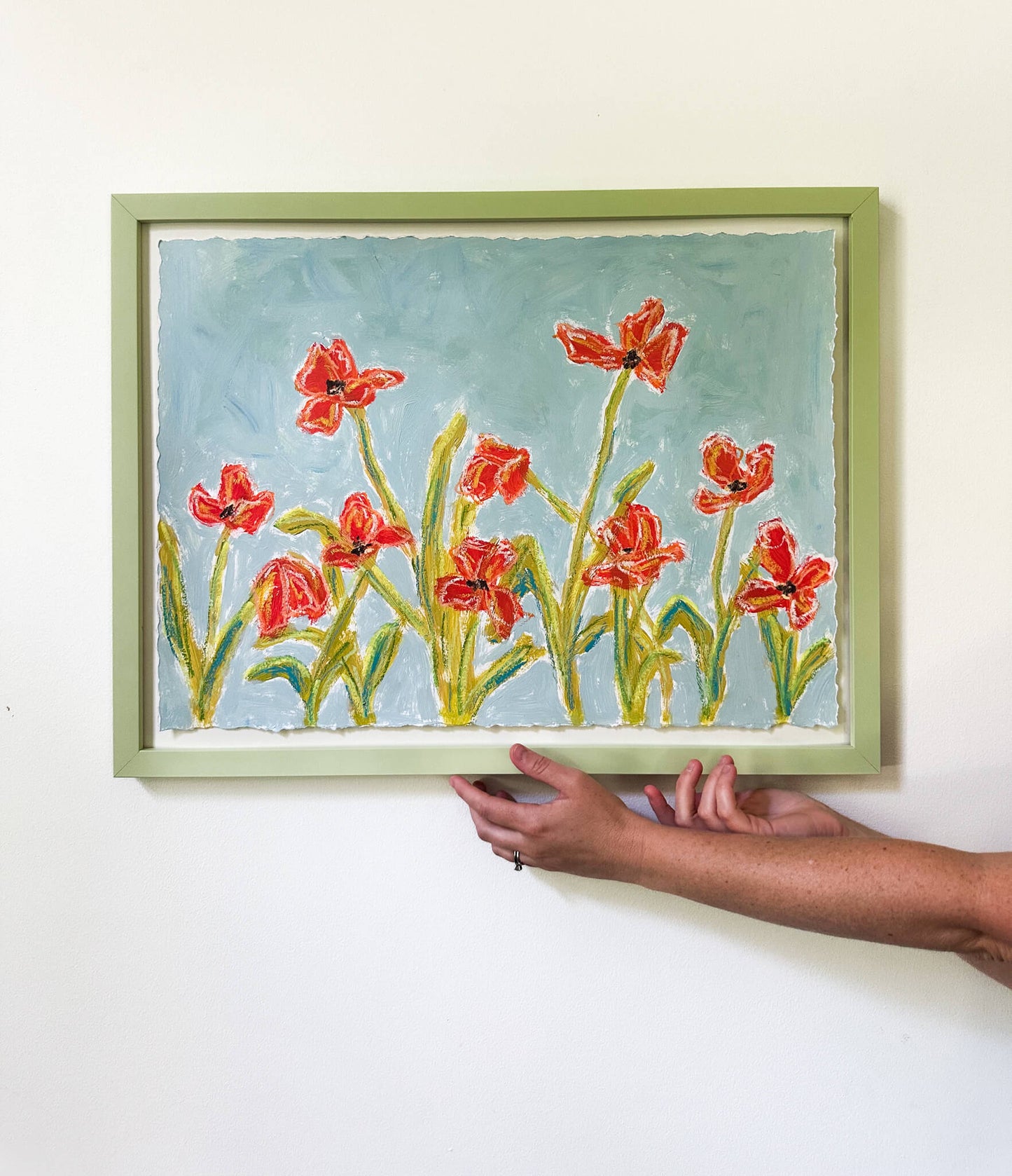 Framed artwork of red flowers held by a person against a white background
