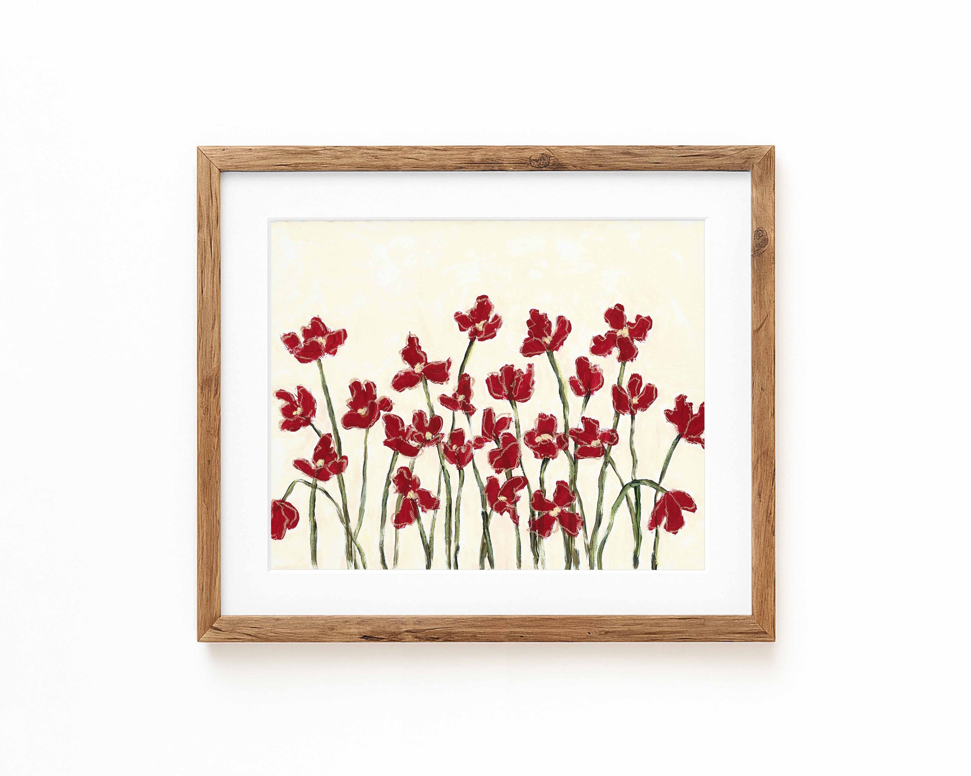 An art print of deep red flowers on a cream background framed in a natural wood frame and displayed against a white backdrop.