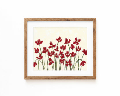 An art print of deep red flowers on a cream background framed in a natural wood frame and displayed against a white backdrop.