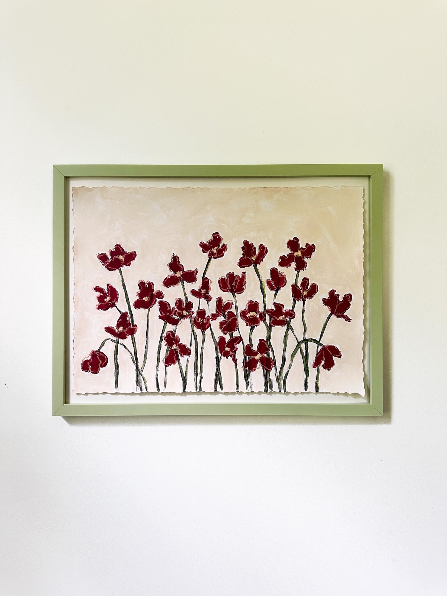 a painting of red flowers painting on a beige background framed and hung on a white wall.