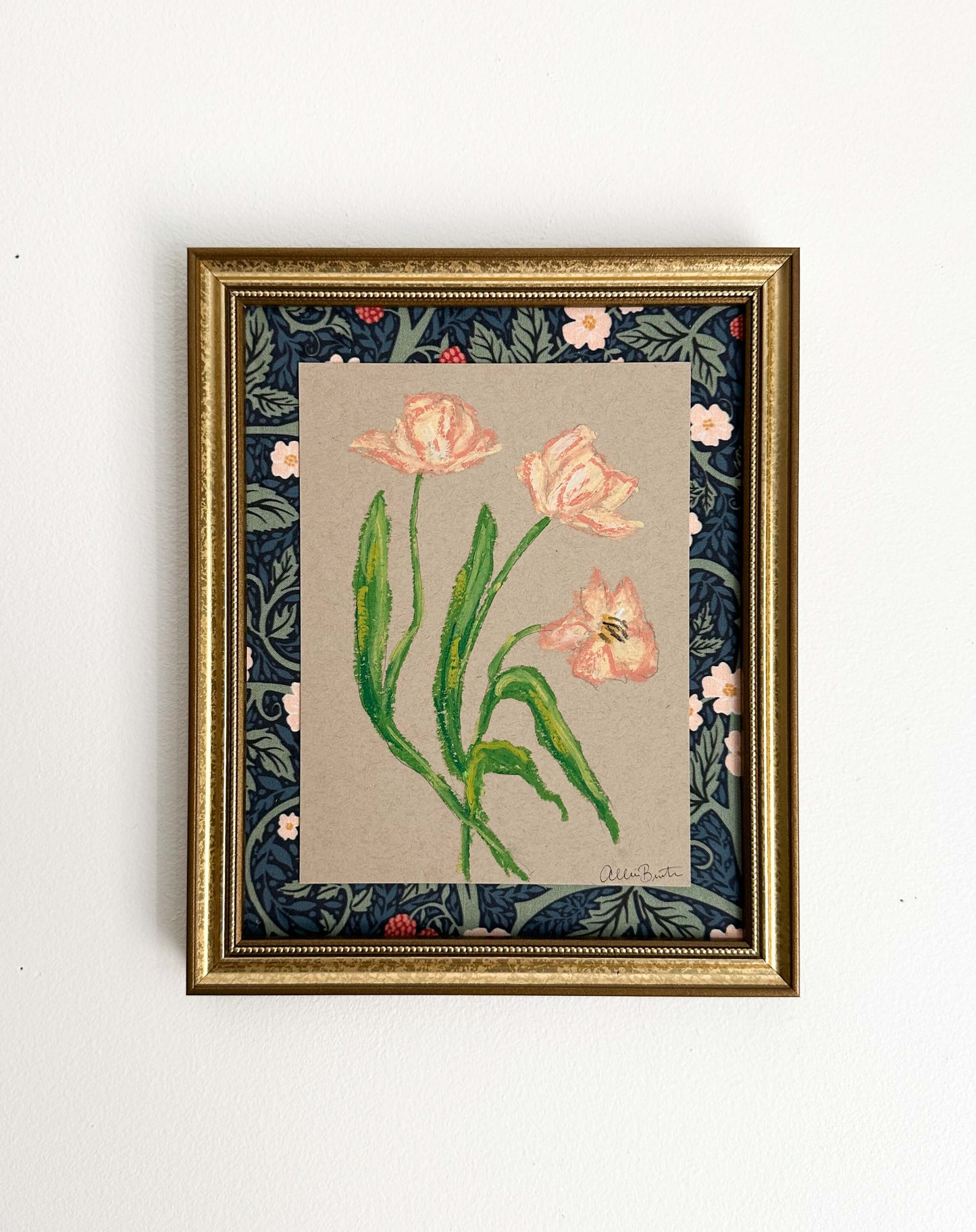 peach florals painted with oil pastels on tan paper, mounted on floral fabric and framed in a gold frame. Painting shown on a white wall