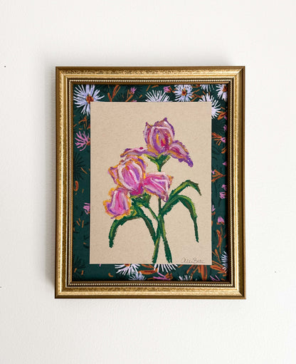 A painting of purple irises on tan paper mounted on dark floral fabric. The painting is in a gold frame and shown on a white wall.