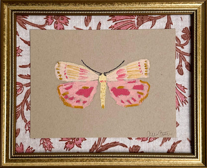 a pink and yellow butterfly painting on tan paper, mounted on pink and tan floral fabric and framed in a gold frame.
