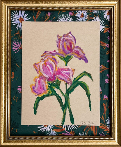 A painting of purple irises on tan paper mounted on dark floral fabric. The painting is in a gold frame.