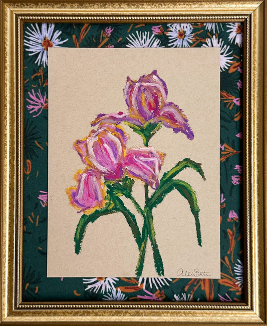 A painting of purple irises on tan paper mounted on dark floral fabric. The painting is in a gold frame.