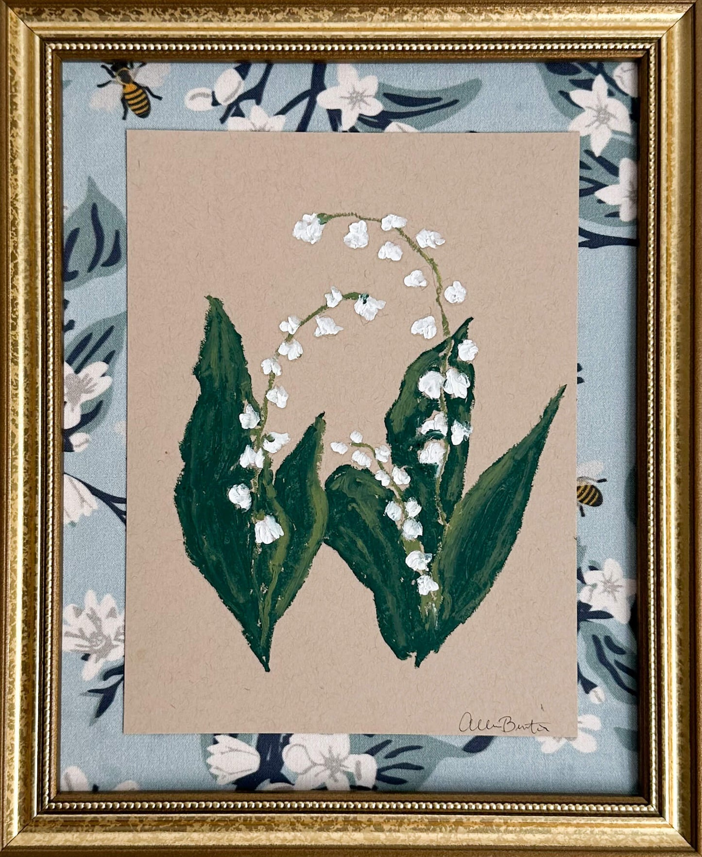 painting of lily of the valley flower on tan toned paper, framed in a gold frame and mounted on a blue floral fabric