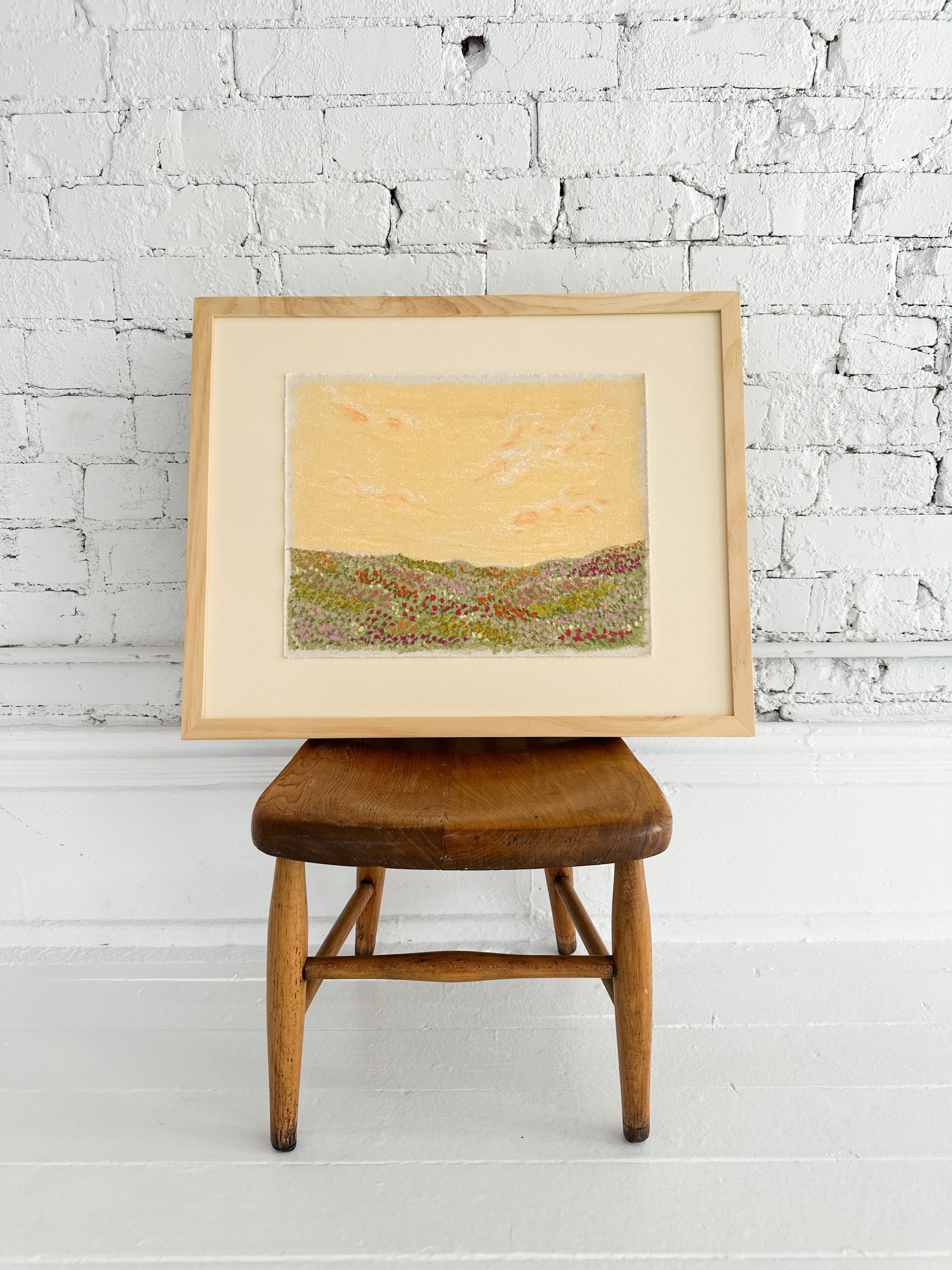 Framed artwork on a wooden stool against a white brick wall.