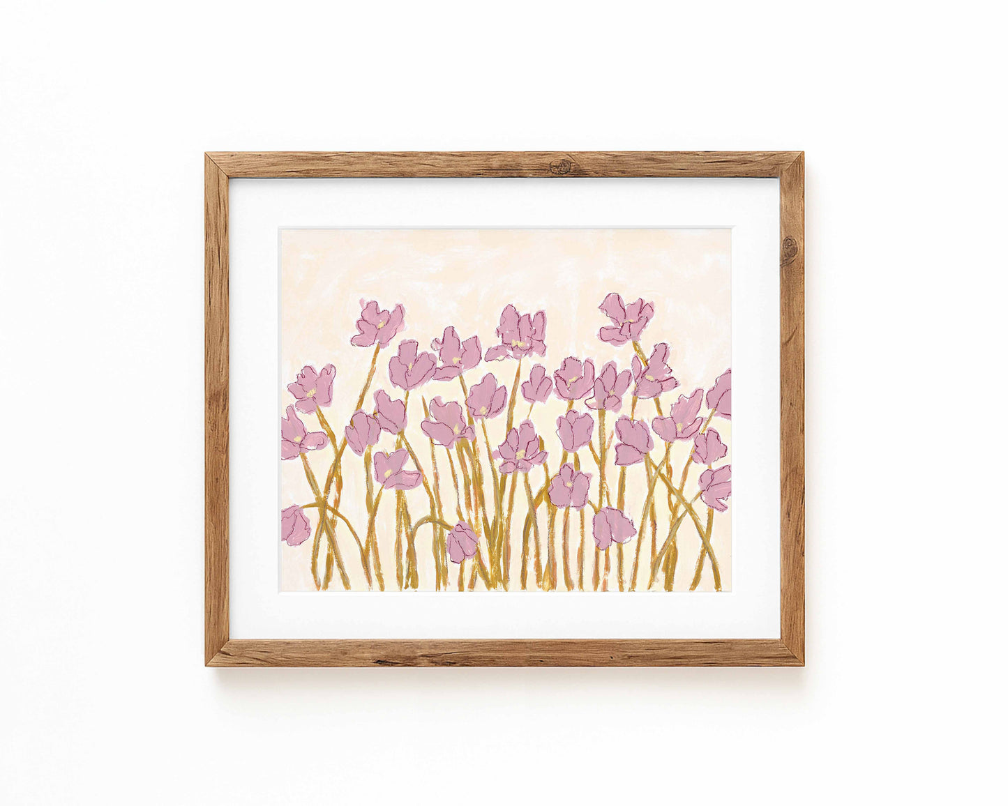An art print of pink flowers on a cream background framed in a natural wood frame and displayed against a white backdrop.