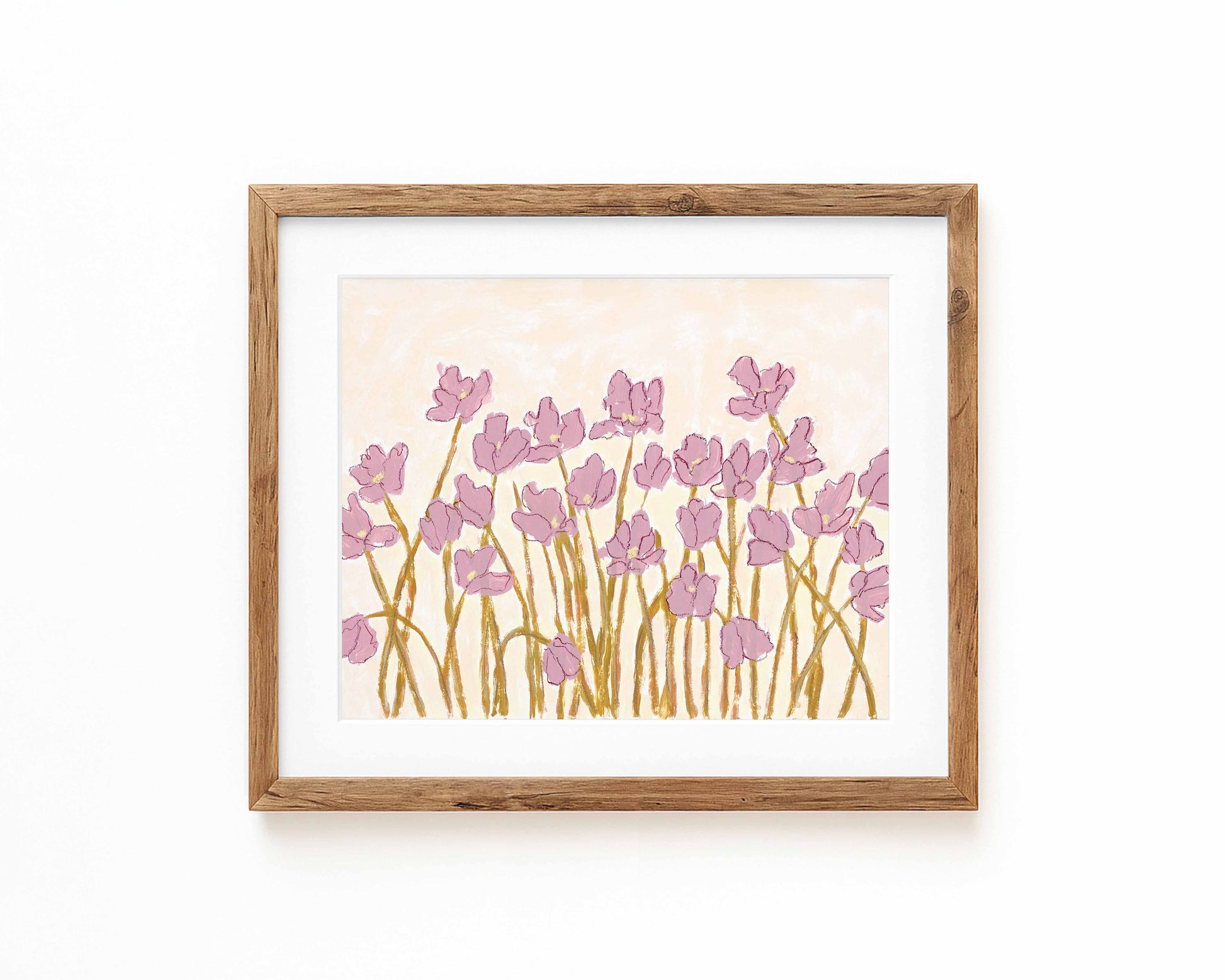 An art print of pink flowers on a cream background framed in a natural wood frame and displayed against a white backdrop.