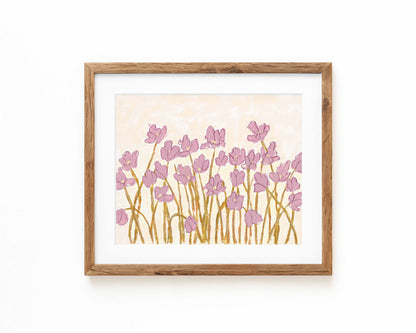 An art print of pink flowers on a cream background framed in a natural wood frame and displayed against a white backdrop.