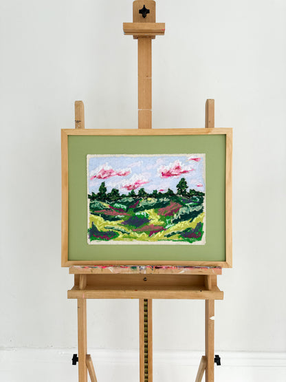 Painting of a landscape on a wooden easel against a white background