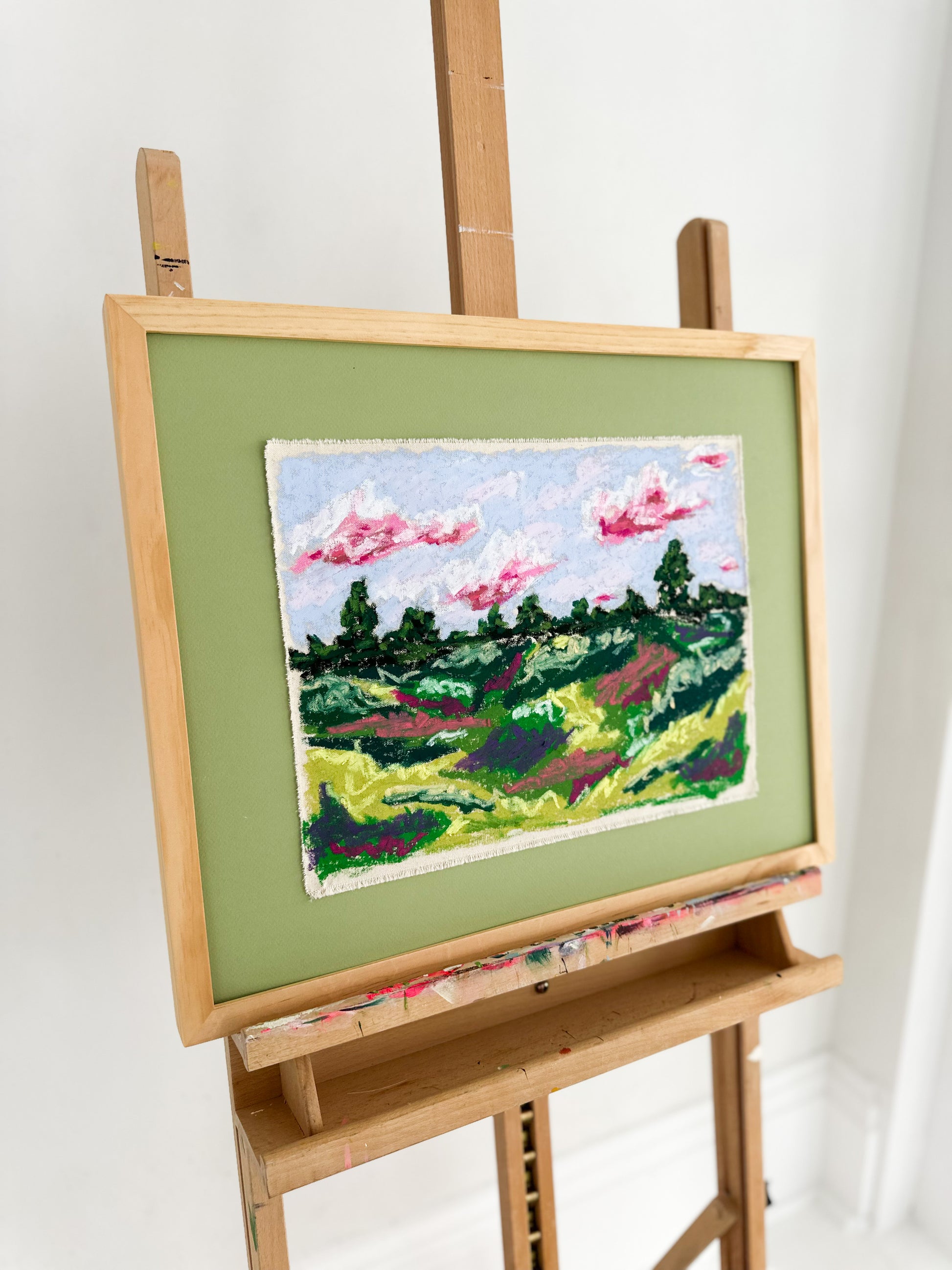 Painting of a landscape on a wooden easel against a white background