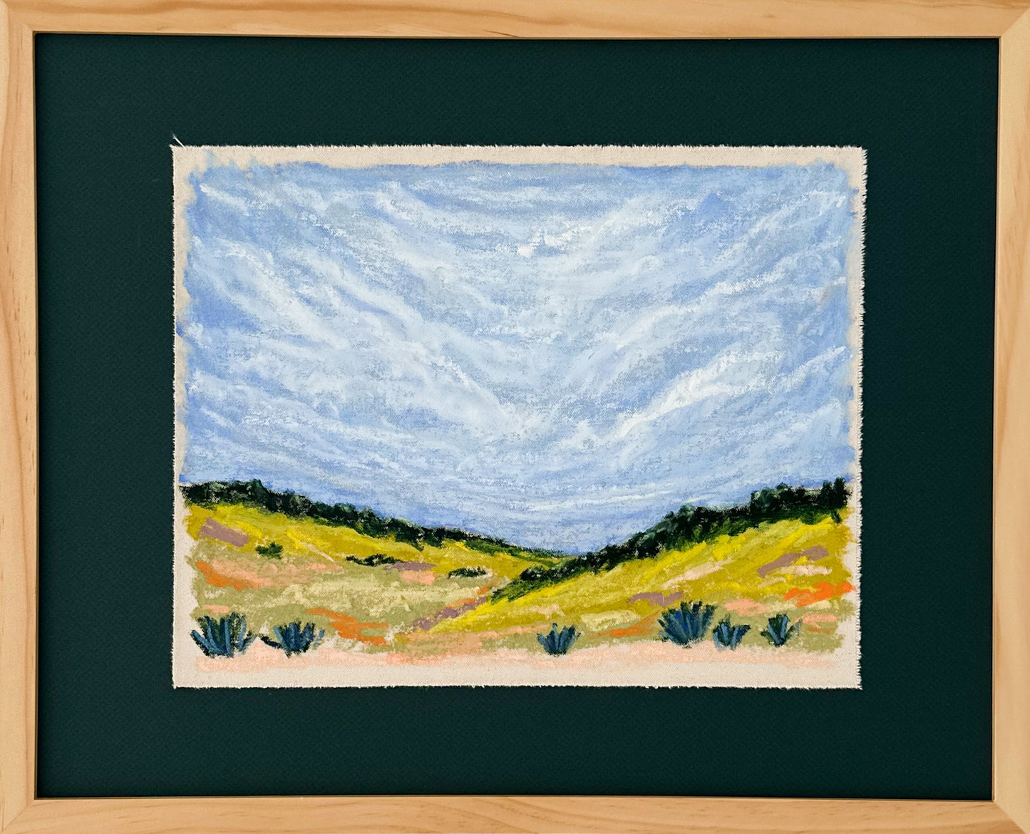 Framed artwork of a landscape with a blue sky and green fields.