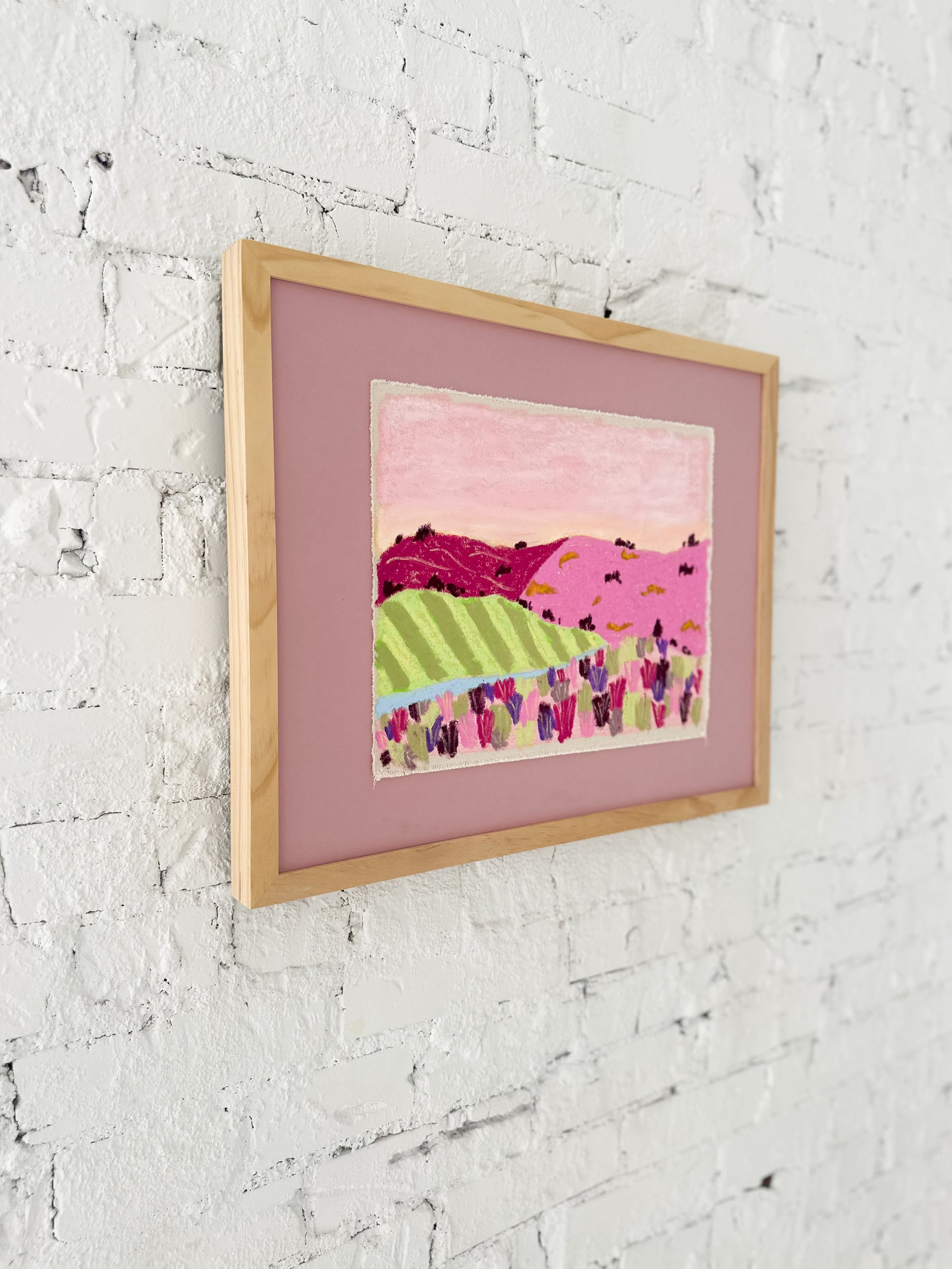 Framed artwork with a colorful landscape scene on a white textured wall