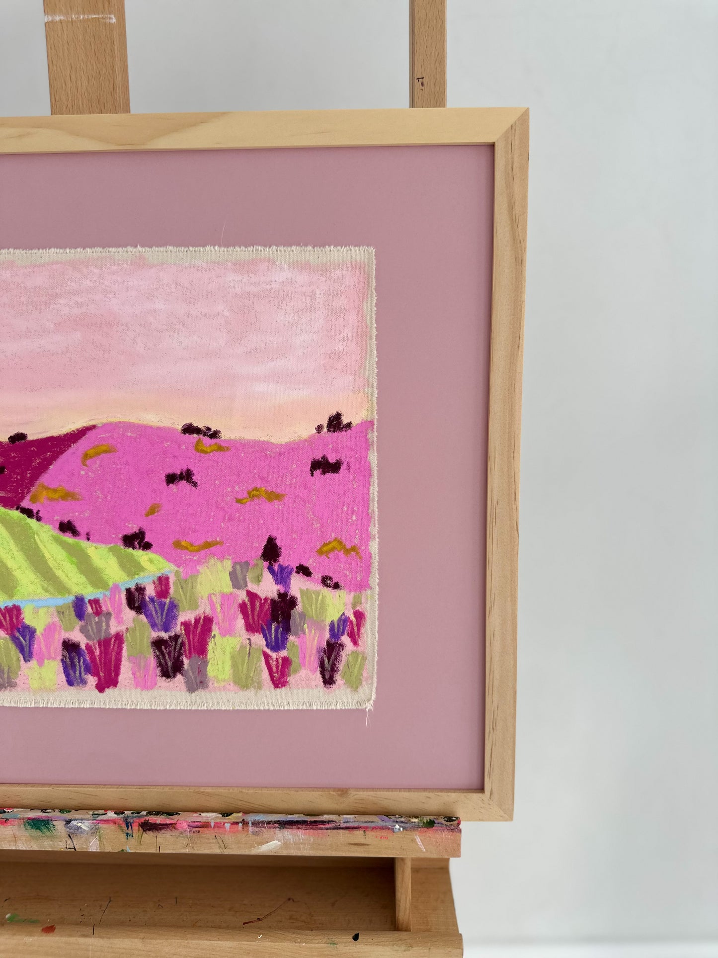 Framed landscape artwork on an easel with a pink background