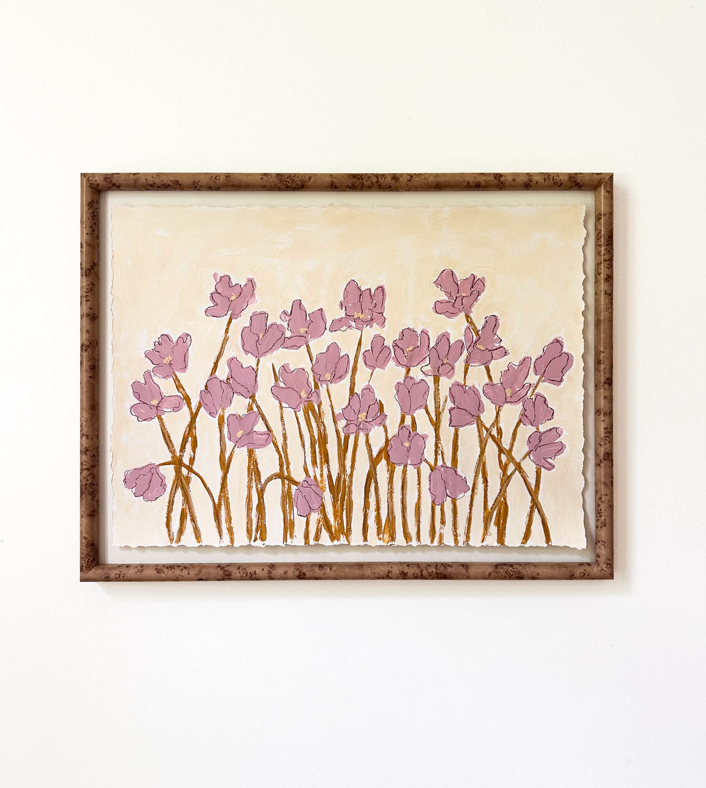 a framed painting of mauve flowers with yellow stems painted on a beige background and hung on a white wall.