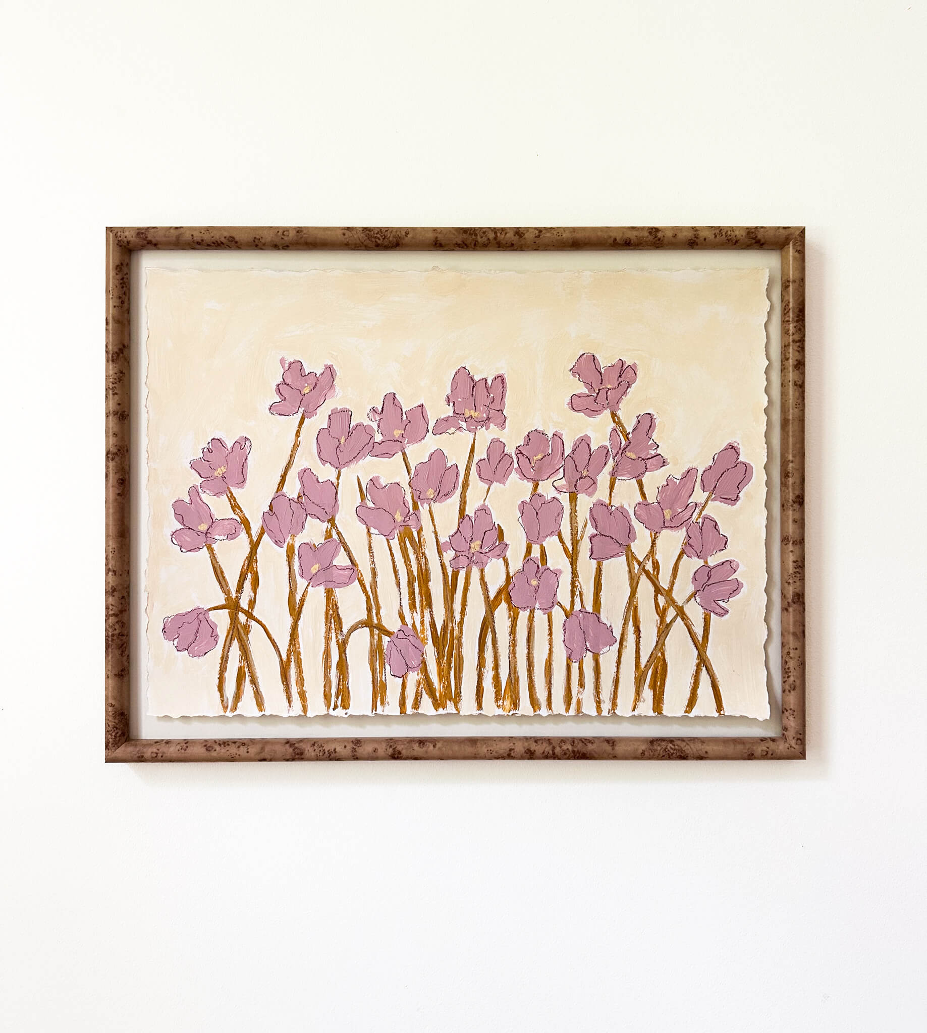 a framed painting of mauve flowers with yellow stems painted on a beige background and hung on a white wall.