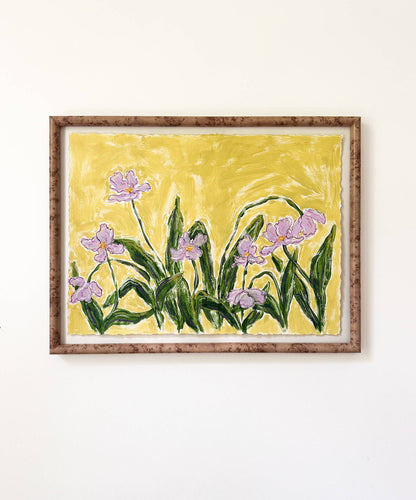 a framed painting of light purple flowers with green stems painted on a bright yellowish green background and hung on a white wall.
