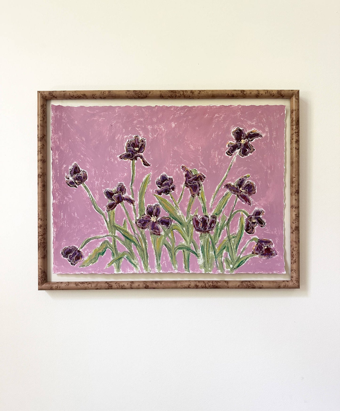 a framed painting of dark purple flowers with green stems painted on a light purple background and hung on a white wall.