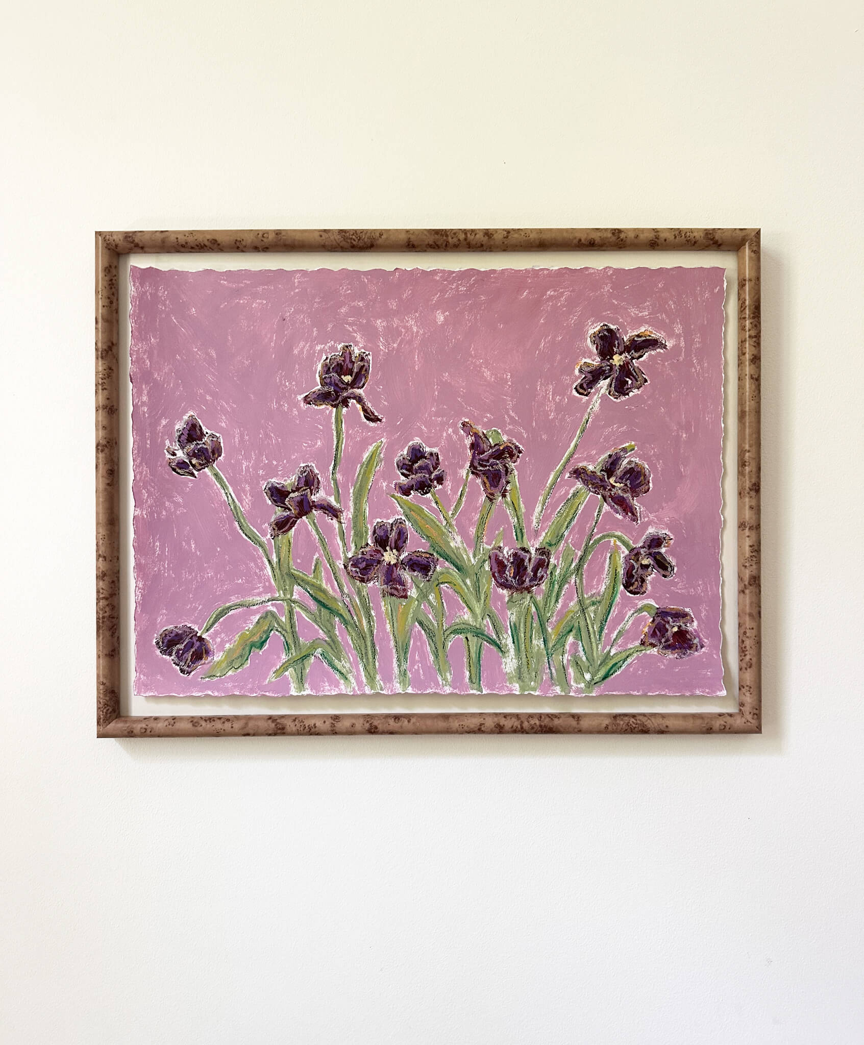 a framed painting of dark purple flowers with green stems painted on a light purple background and hung on a white wall.