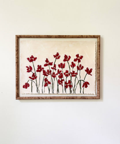 a framed painting of dark red flowers with green stems painted on a beige background and hung on a white wall.