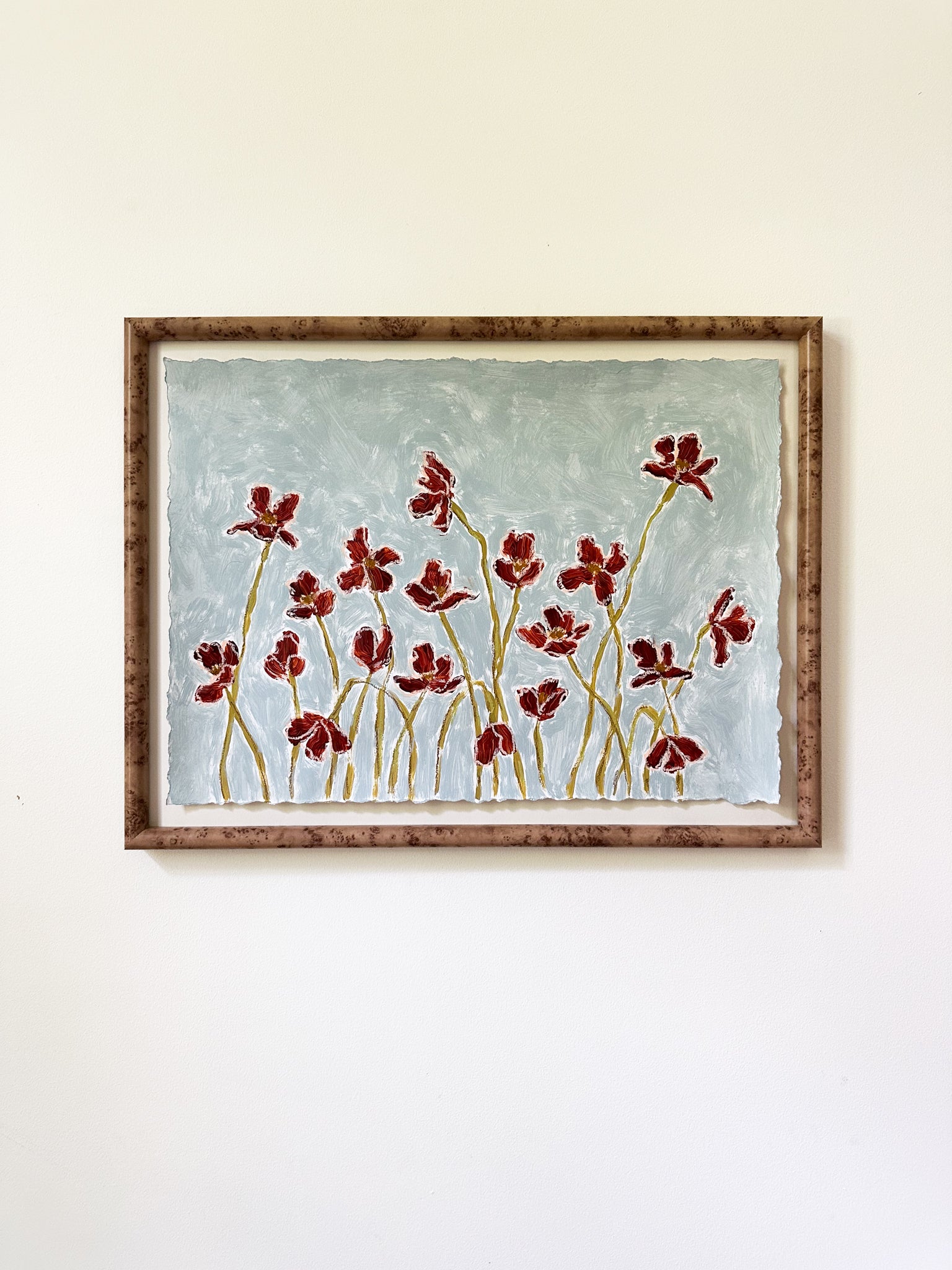 deep blue flowers painted on a dusty blue background framed and hung on a white wall